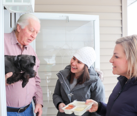 Two women delivery a meal to a man holding a dog