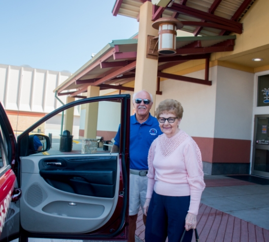 Man helping elderly woman into ride service vehicle